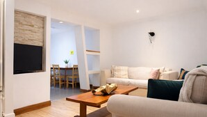 Un salon comprenant un canapé, une table basse, un téléviseur fixé au mur, un coin repas avec une table et des chaises, et un escalier menant à une autre pièce.