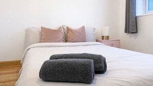 Un lit bien fait, avec du linge de lit blanc et deux serviettes enroulées, une lampe de chevet et une table de chevet avec une lampe.