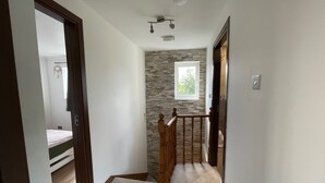 Un couloir avec un escalier en bois, un mur en pierre et une fenêtre.
