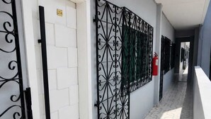 A corridor with a white door, a black metal gate, and a fire extinguisher on the wall. - Feel at Home in Belém – Cozy & Fully Equipped Apartment in Guamá (Guamá, Belém)