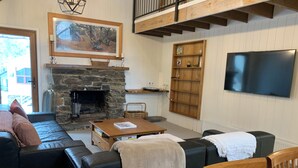 A cozy living room with a stone fireplace, a large painting, a wooden bookshelf, and a flat-screen TV. - Tower House Two Chalet (Dinner Plain)