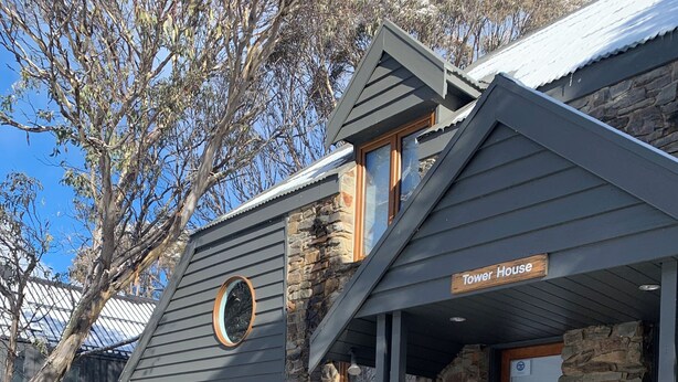 A building named "Tower House" with a stone exterior, a wooden door, and a sign indicating "Unit 2" and "3 CORSLEY." - Tower House Two Chalet (Dinner Plain)