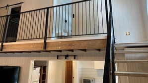 A multi-level interior with a wooden balcony railing, a kitchen area with a microwave, and a visible door leading to another room. - Tower House Two Chalet (Dinner Plain)