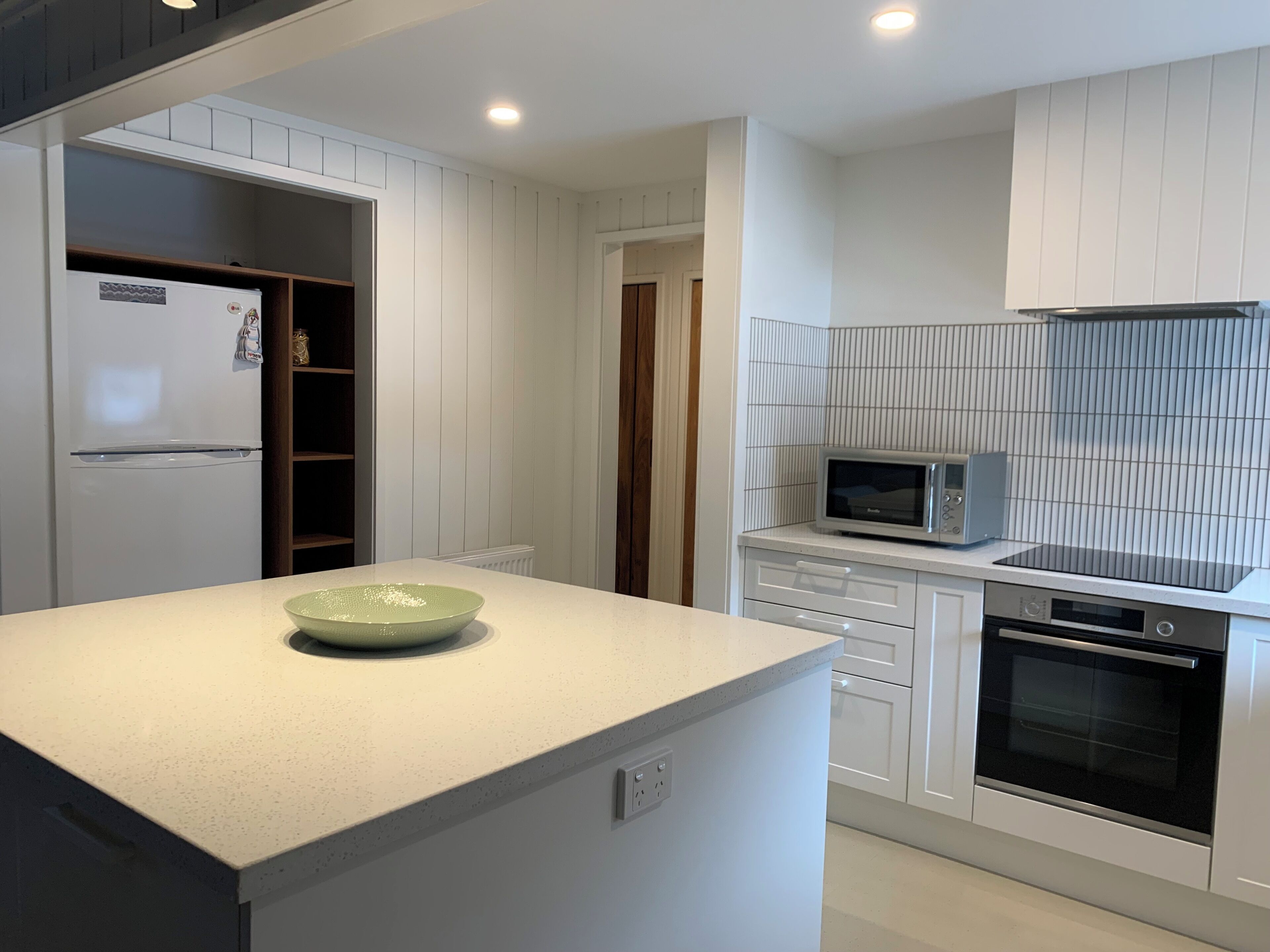 A modern kitchen with white cabinetry, a microwave, an oven, and a bowl on the countertop.