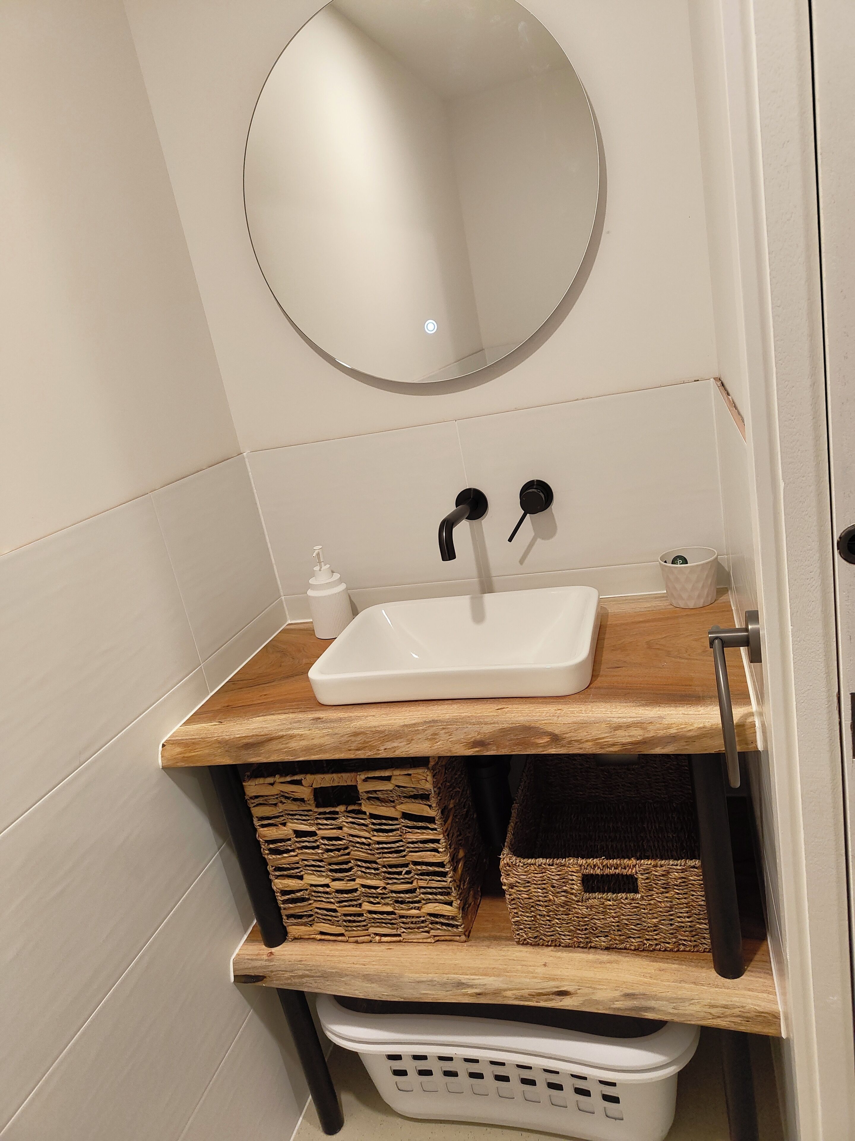 Een badkamer met een witte wastafel, een ronde spiegel en een houten plank met manden.