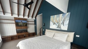 A bedroom with a large bed, wooden entertainment unit, and a ceiling fan. - Tower House Two Chalet (Dinner Plain)