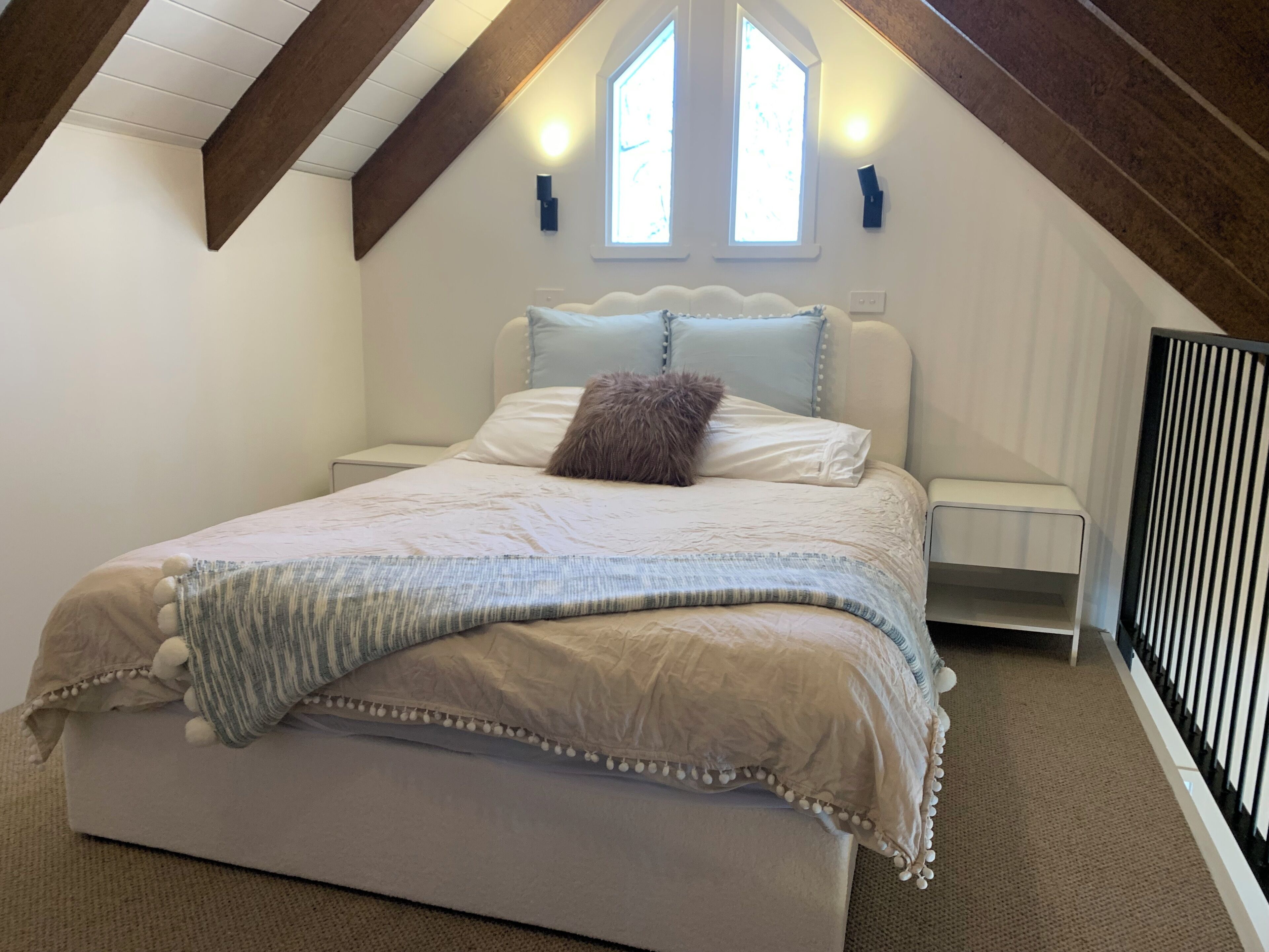 A bedroom with a large bed, a nightstand, two wall-mounted lights, and a window with a view.