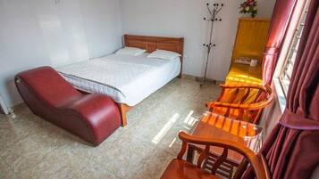 A bedroom with a bed, a red leather chair, a wooden table, and a floor lamp.