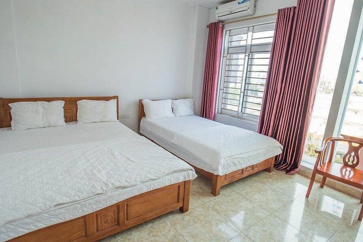 A room with two wooden beds, a window with curtains, and a chair.