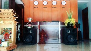 A reception desk with a wooden backdrop labeled with city names. There are two large speakers on either side, a small statue in front, and a vase with flowers to the right. - An Binh 2 Hotel BG - by BAY LUXURY (Bac Giang)