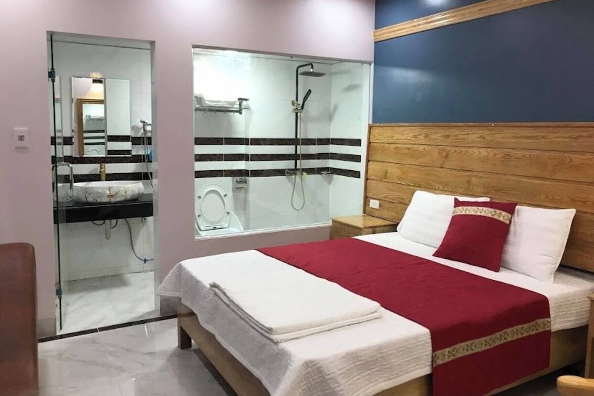 A modern bedroom with a glass shower enclosure, a wooden headboard, and a neatly made bed with a red and white bedspread.
