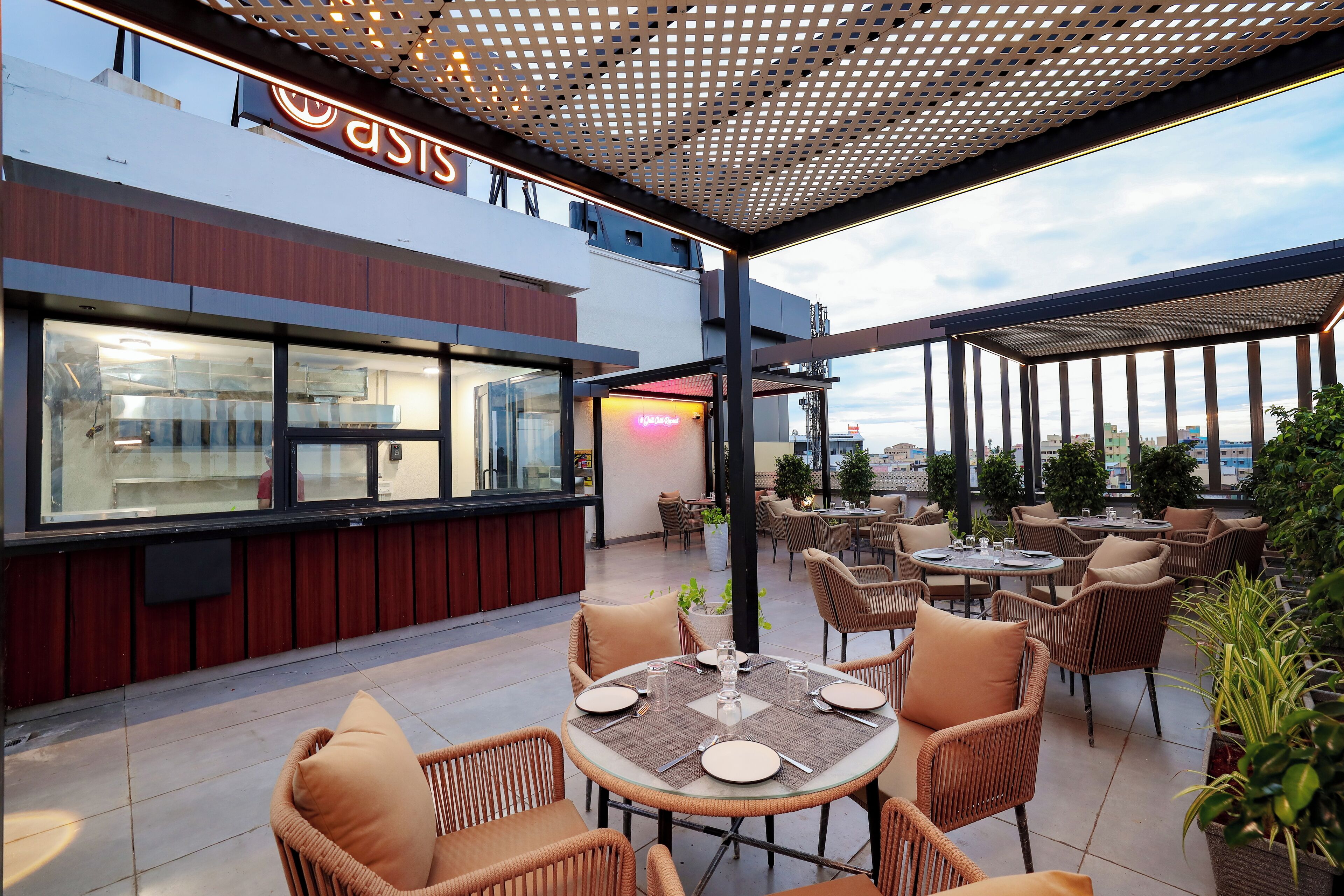 Un espace de restauration en plein air avec des chaises et des tables en osier, un restaurant avec une enseigne au néon et une vue sur la ville.