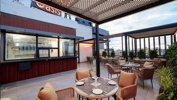 Un espace de restauration en plein air avec des chaises et des tables en osier, un restaurant avec une enseigne au néon et une vue sur la ville.