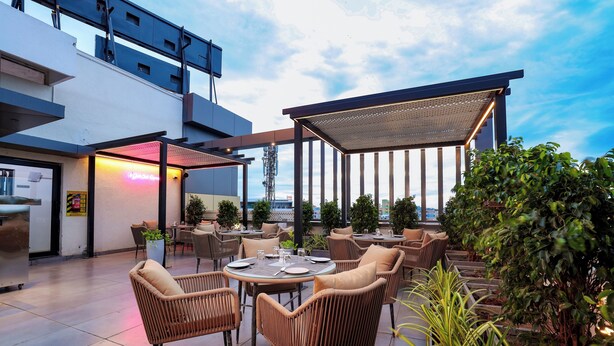An outdoor seating area with wicker chairs and tables, a covered section, and potted plants. - Sathyam Oasis  (Tiruchirappalli)