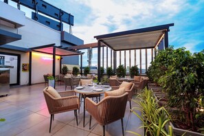 An outdoor seating area with wicker chairs and tables, a covered section, and potted plants. - Sathyam Oasis (Tiruchirappalli)