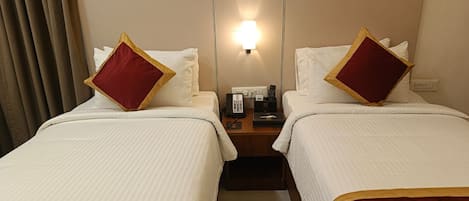 A hotel room with two beds, a nightstand with a phone and a lamp, and a window with curtains.