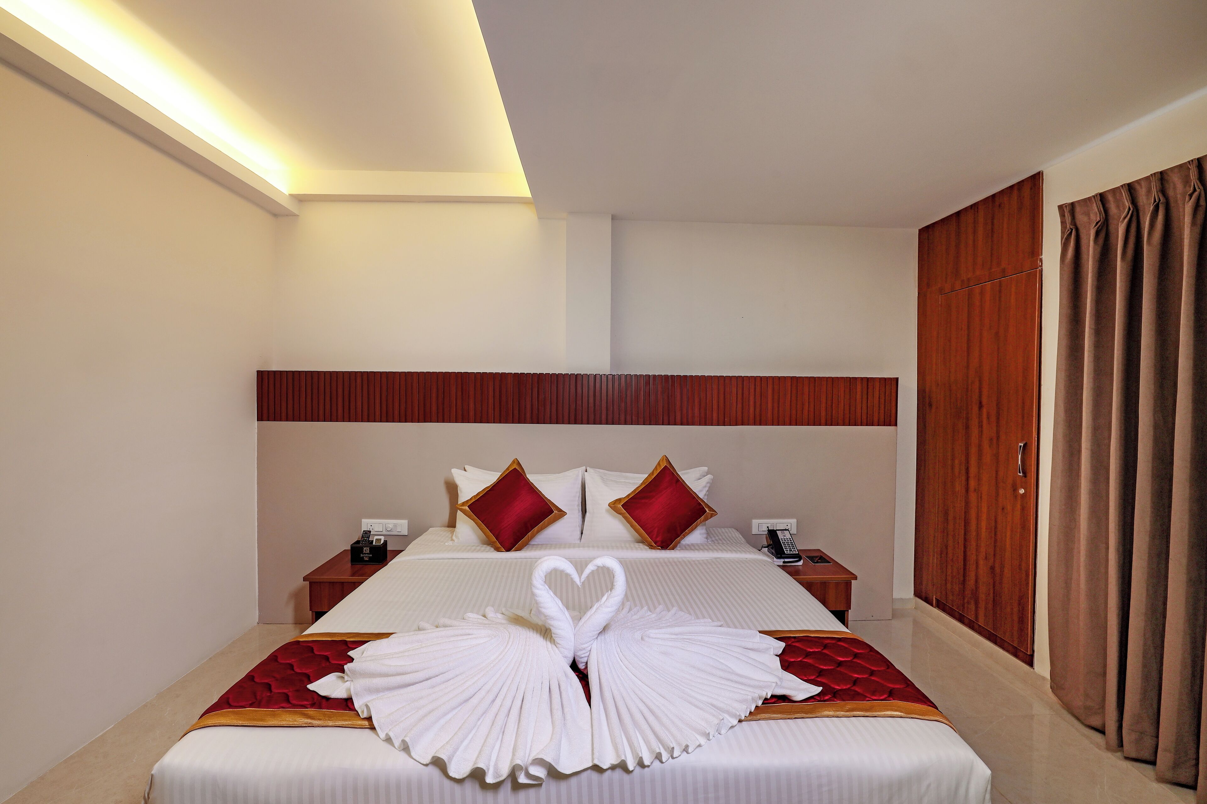 A hotel room with a neatly made bed, a wooden headboard, a bedside table with a phone, and a wardrobe.