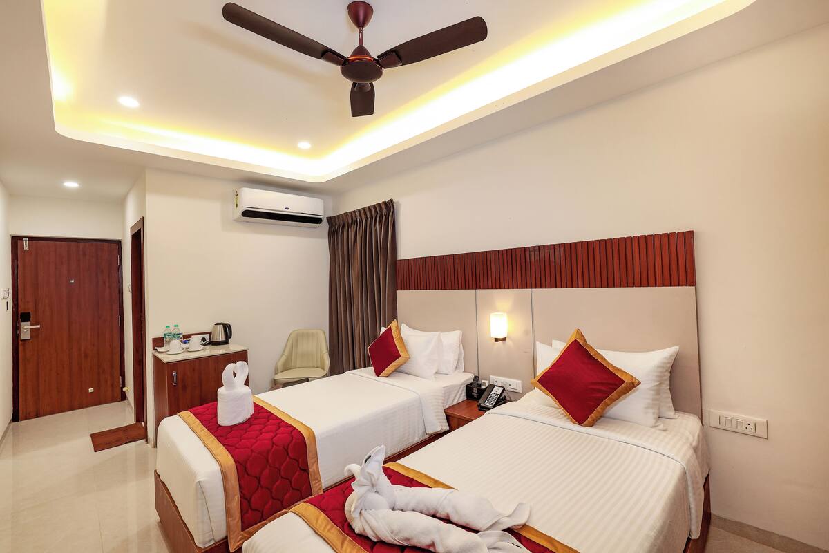 Ein Hotelzimmer mit zwei Betten, einem Deckenventilator, einer Klimaanlage, einem Nachttisch mit Telefon und einem Schreibtisch mit Wasserkocher und Tassen.