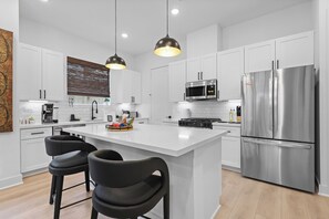 A modern kitchen with white cabinets, stainless steel appliances, and black bar stools. - Gallery of The Motherland With Private Sauna and Hot Tub (Houston)
