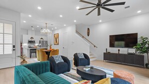 Un salon moderne avec un canapé de couleur turquoise, des fauteuils foncés, une table basse et un escalier menant à un niveau supérieur.