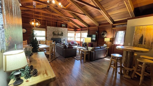 Una cabaña espaciosa con techos altos, vigas de madera, chimenea, televisor y comedor con un árbol de Navidad.