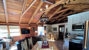 Una cocina amplia con vigas de madera, un comedor con sillas rústicas, y una cocina moderna que incluye un refrigerador y un microondas.