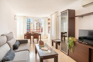 A modern living room with a sofa, coffee table, TV, and dining area.