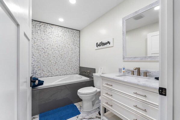 A modern bathroom with a bathtub, toilet, and vanity with drawers.