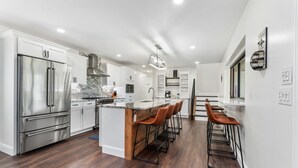 Une cuisine moderne dotée d’appareils électroménagers en acier inoxydable, d’un plan de travail en marbre et d’un îlot central en bois avec des tabourets de bar.