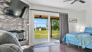 Une chambre moderne avec une cheminée en pierre, un lit avec une literie bleue et une vue sur une cour verdoyante.