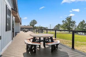 En træterrasse med picnicborde og gelænder, med udsigt over en græsplæne og en vej.