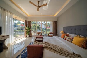 A spacious bedroom with a large bed, a ceiling fan, a TV, and a balcony with outdoor seating. - Perfectstayz Koko Maya (Morjim)