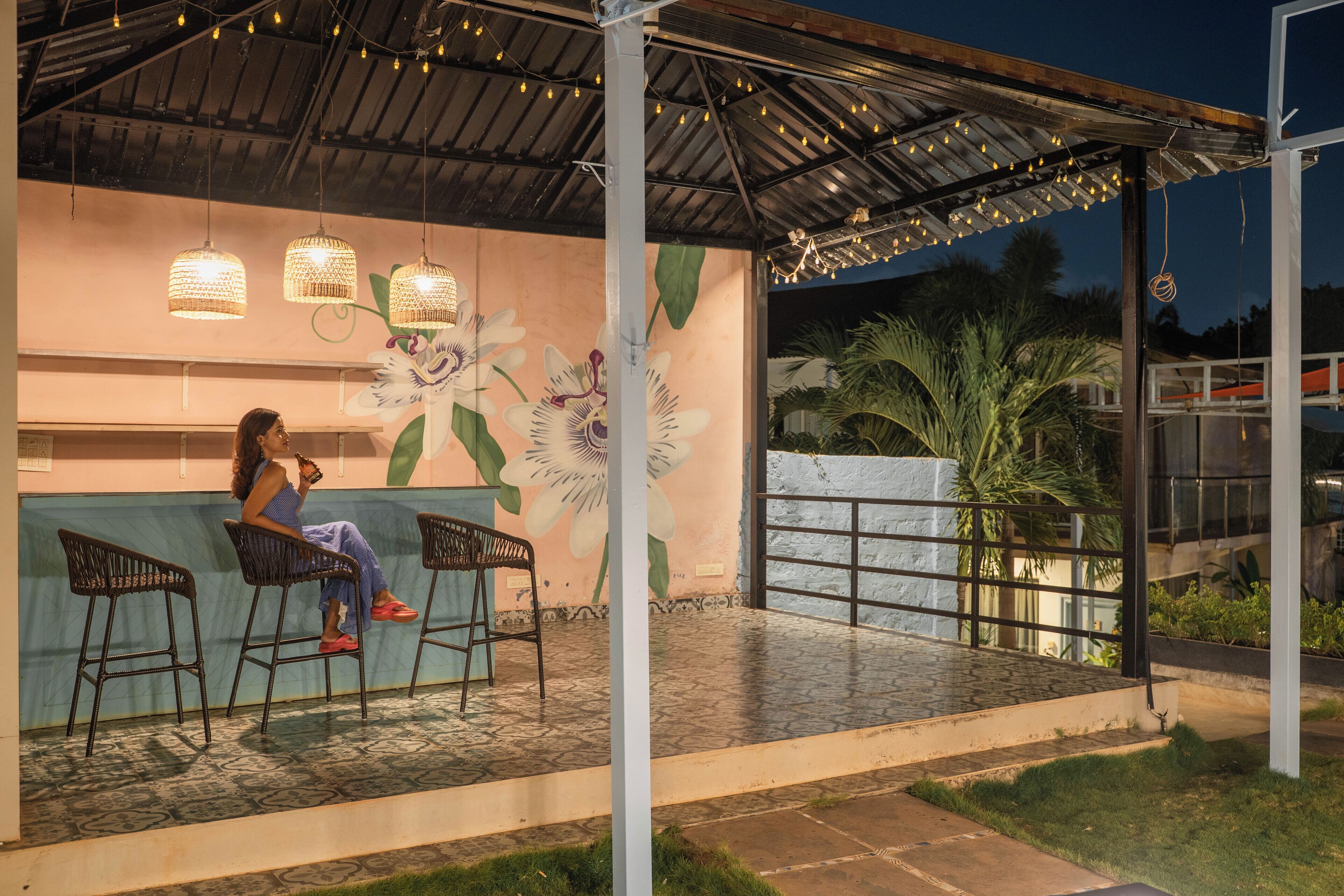 A covered outdoor seating area with a mural of flowers, a bar counter, and hanging lights.