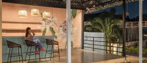 A covered outdoor seating area with a mural of flowers, a bar counter, and hanging lights.