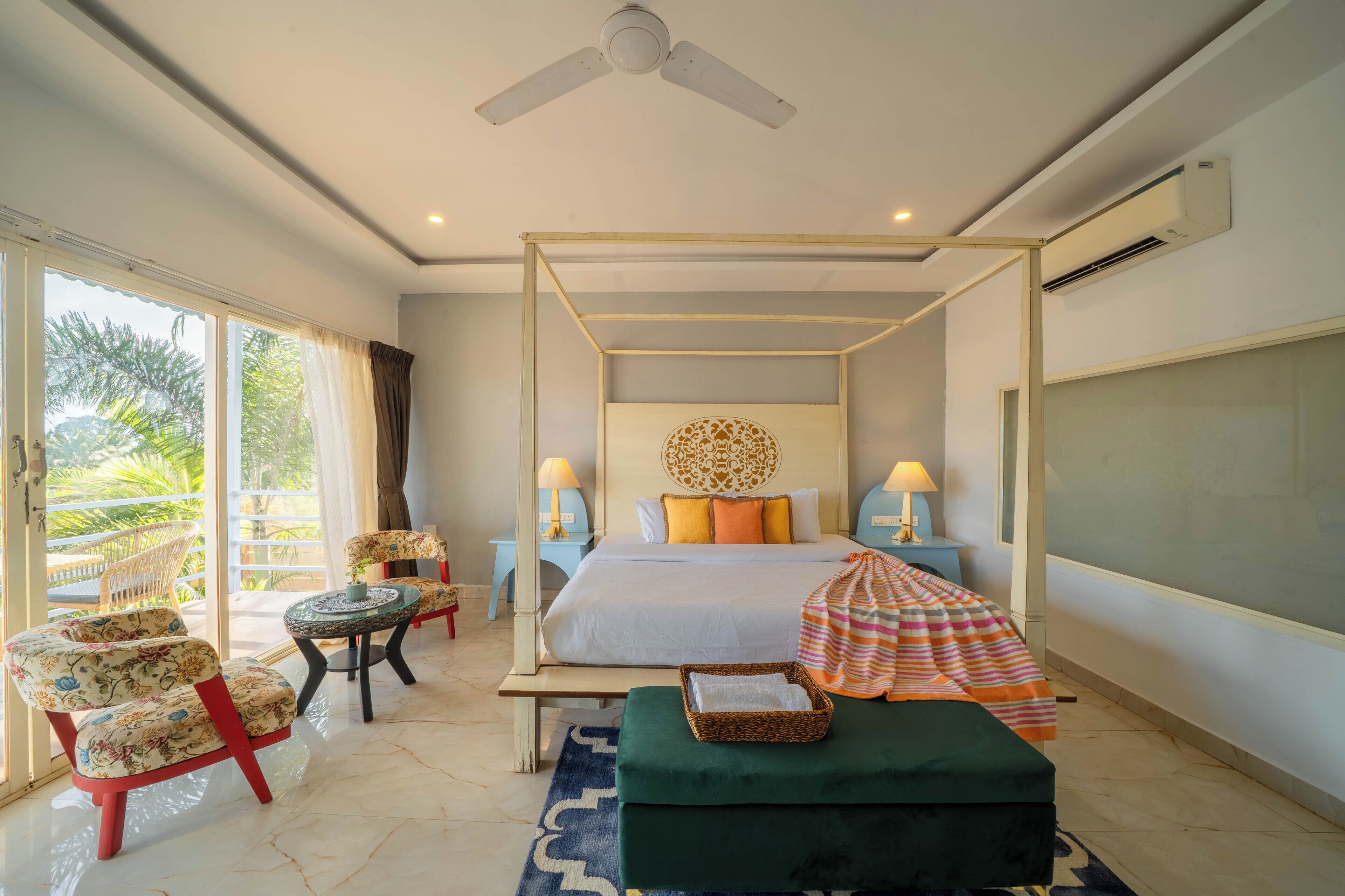 A bedroom with a four-poster bed, a balcony with chairs, a small round table, and a green ottoman.