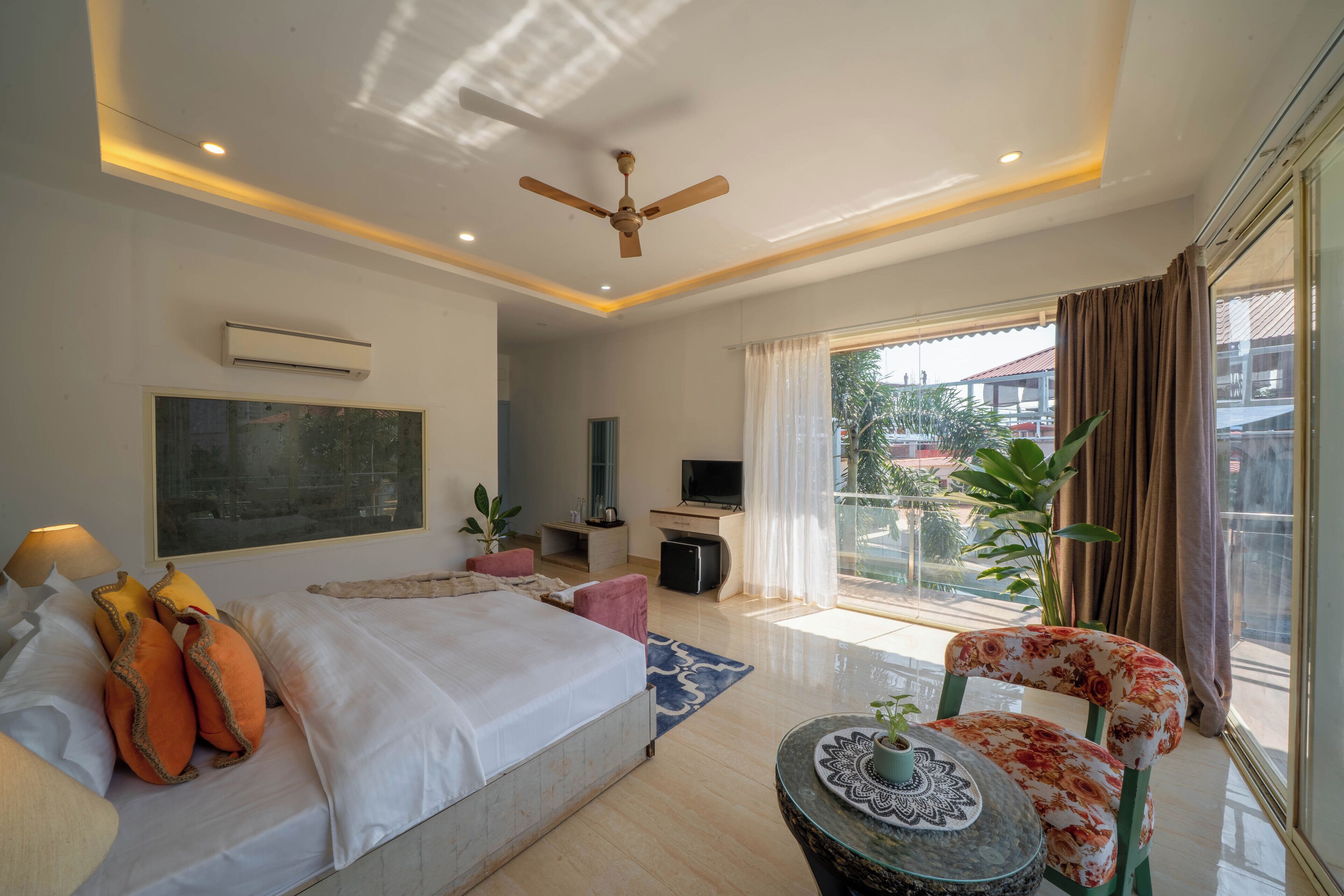 A modern hotel room with a large bed, a ceiling fan, a TV, and a balcony with curtains.