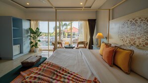 A hotel room with a large bed, a desk, a chair, a potted plant, and a view of the outside. - Perfectstayz Koko Maya (Morjim)