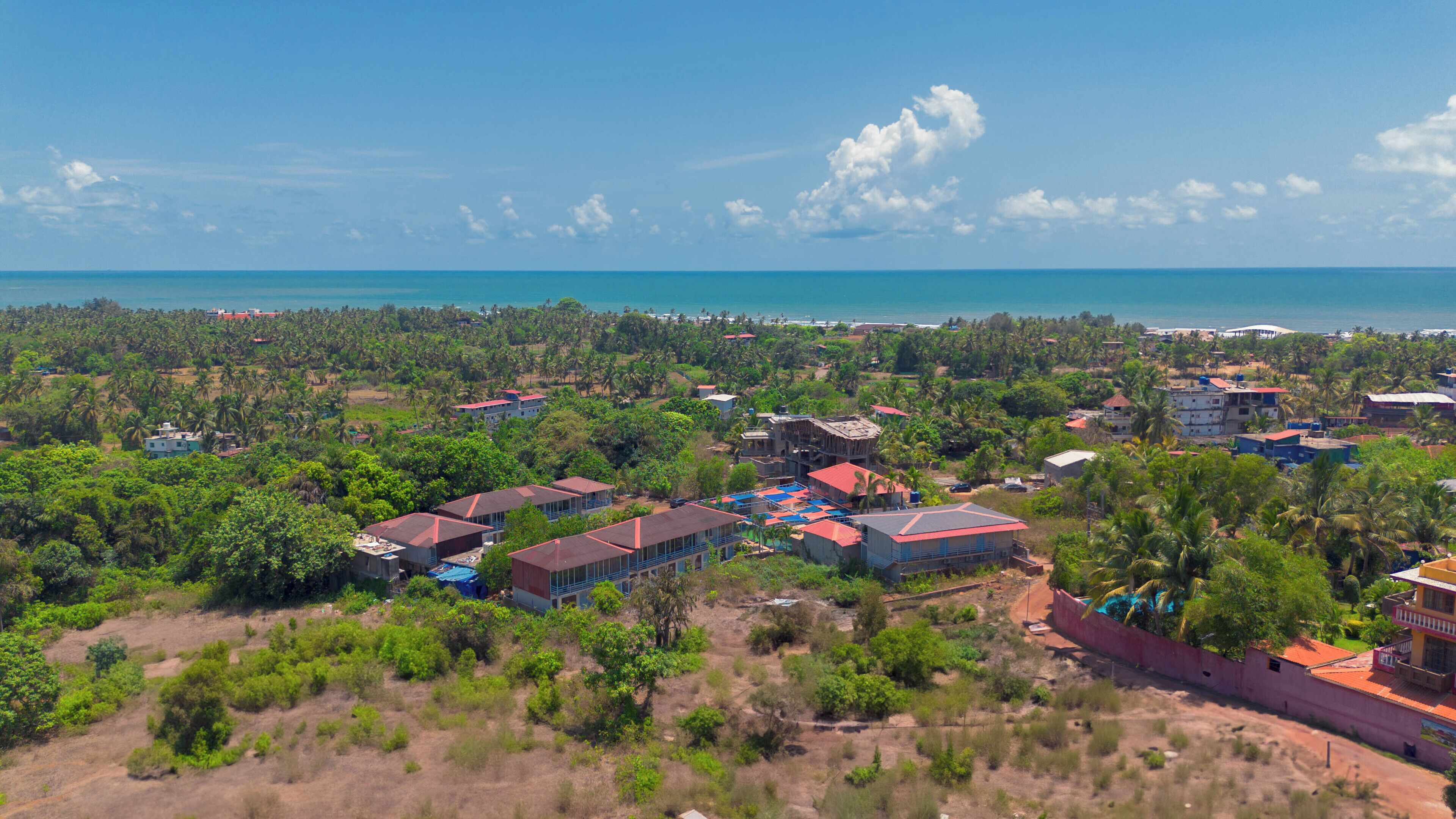 Ein Küstenresort mit mehreren Gebäuden, darunter ein großes Hotel mit Poolanlage, umgeben von üppiger Vegetation und Palmen.