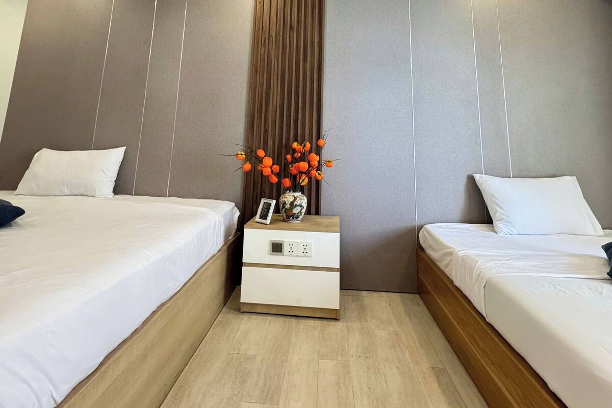 Une chambre d’hôtel moderne avec deux lits, une table de chevet ornée d’un vase de fleurs et un mur décoré de lignes verticales.