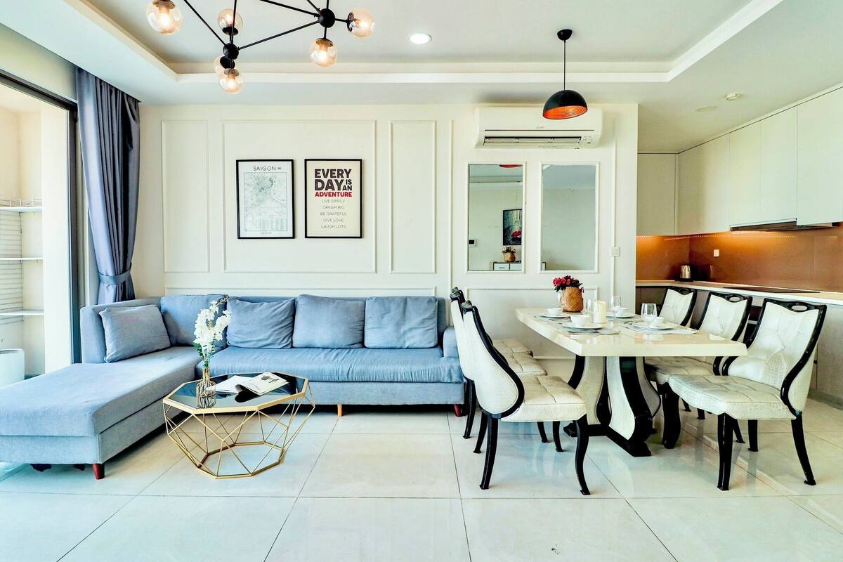 Un salon moderne avec un canapé gris, une table à manger avec des chaises et une table basse ornée d’un vase de fleurs.