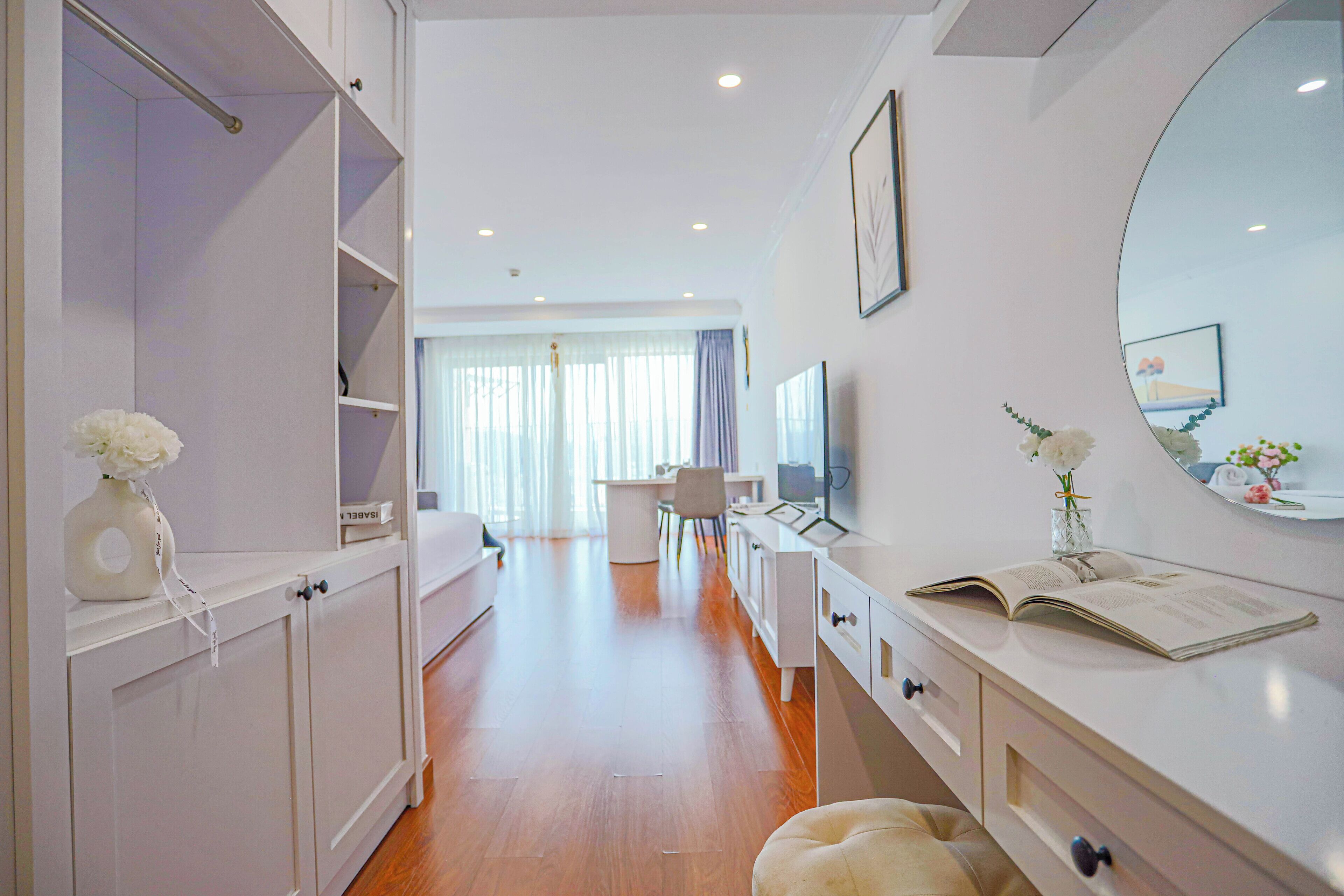 A modern hotel room with a walk-in closet, a vanity with a mirror, and a desk area.