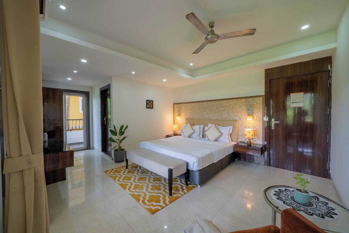 A modern bedroom with a large bed, a ceiling fan, a bedside table with a lamp, and a small table with a plant.