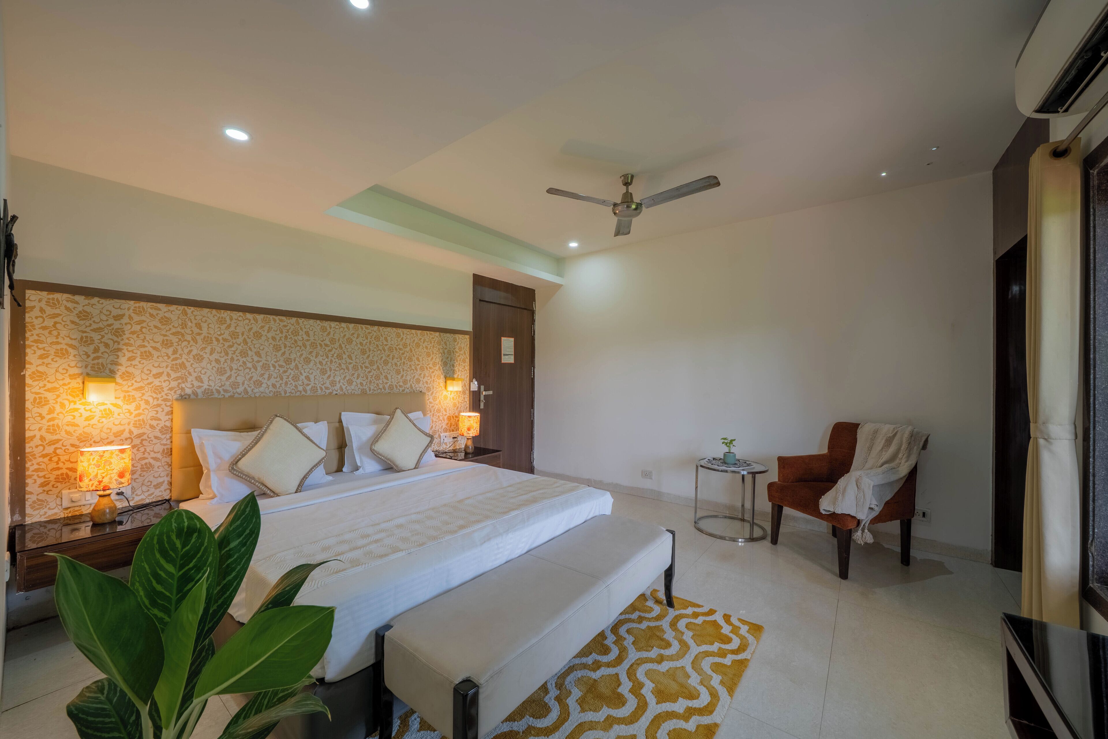 A hotel room with a large bed, a bedside table with a lamp, a chair, and a ceiling fan.
