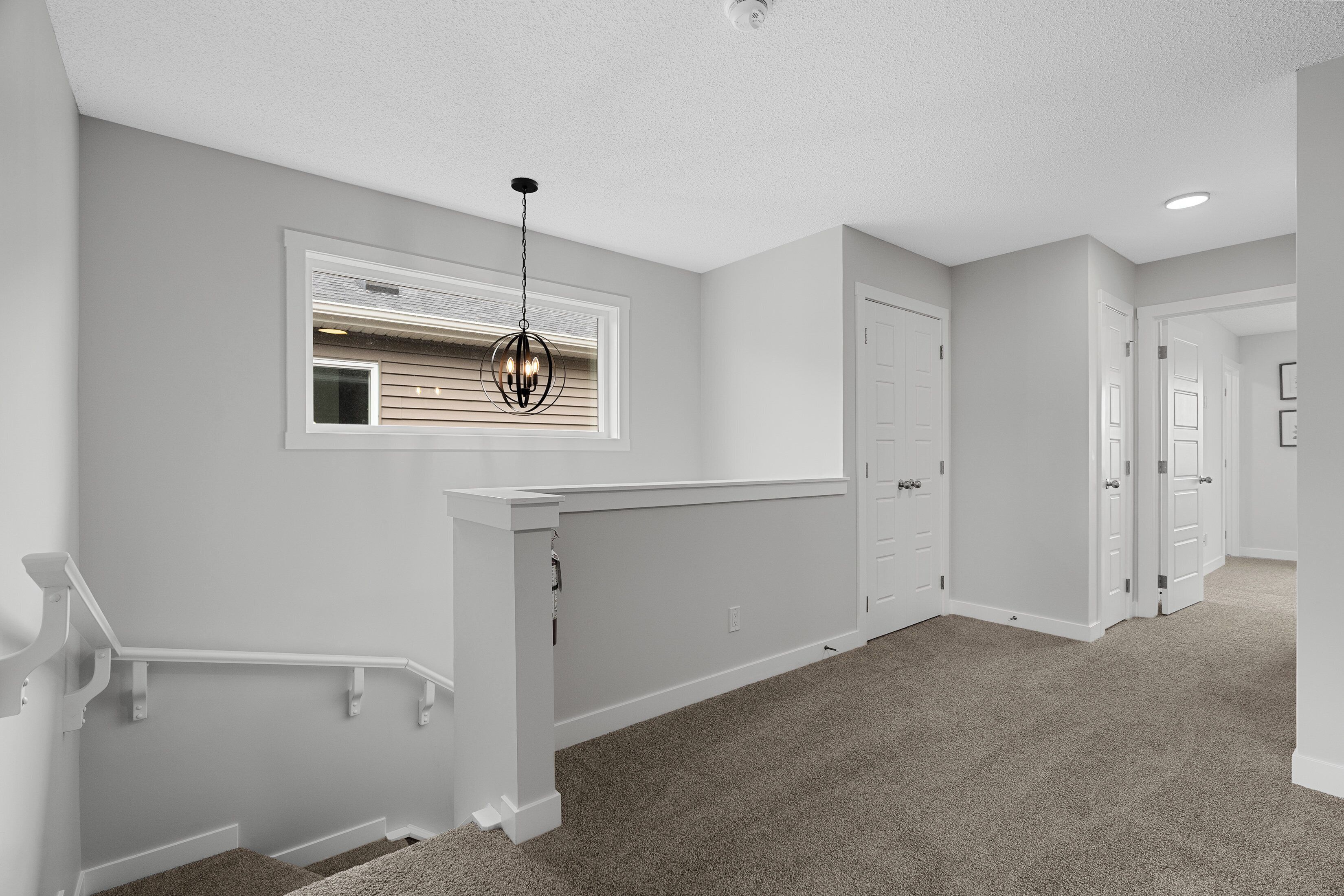 A hallway with a carpeted floor, a staircase with a white handrail, and a ceiling light fixture.