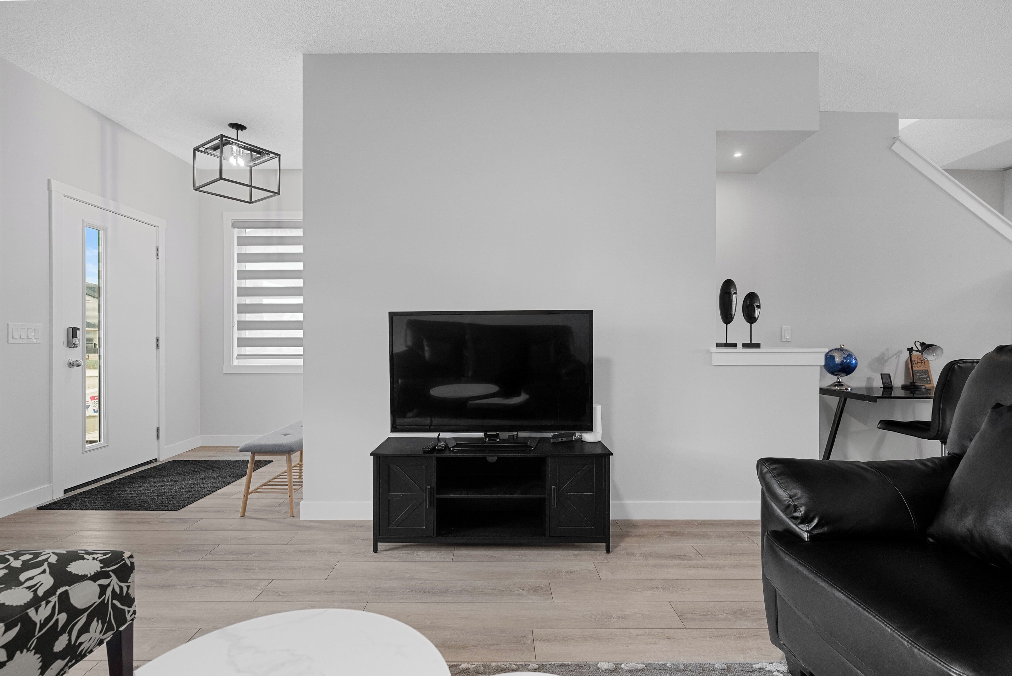 Een moderne woonkamer met een flatscreen televisie op een zwarte tv-meubel, een zwarte leren bank en een witte salontafel.