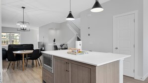 Eine moderne Küche mit Kochinsel, Pendelleuchten und einem Essbereich mit schwarzem Sofa und Stühlen.