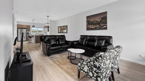 Ein modernes Wohnzimmer mit einem schwarzen Ledersofa, einem gemusterten Sessel, einem Couchtisch und einem Flachbildfernseher.