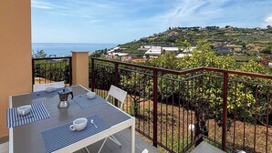 A balcony with a table and chairs, overlooking a coastal landscape with buildings and vineyards. - Galatea by Interhome (Sanremo)