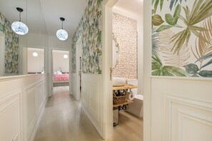 Un couloir avec un miroir, un plancher en bois, un mur à motifs et une salle de bain avec des toilettes et un lavabo.