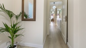Een gang met een kamerplant, een spiegel en een deur naar een andere kamer.